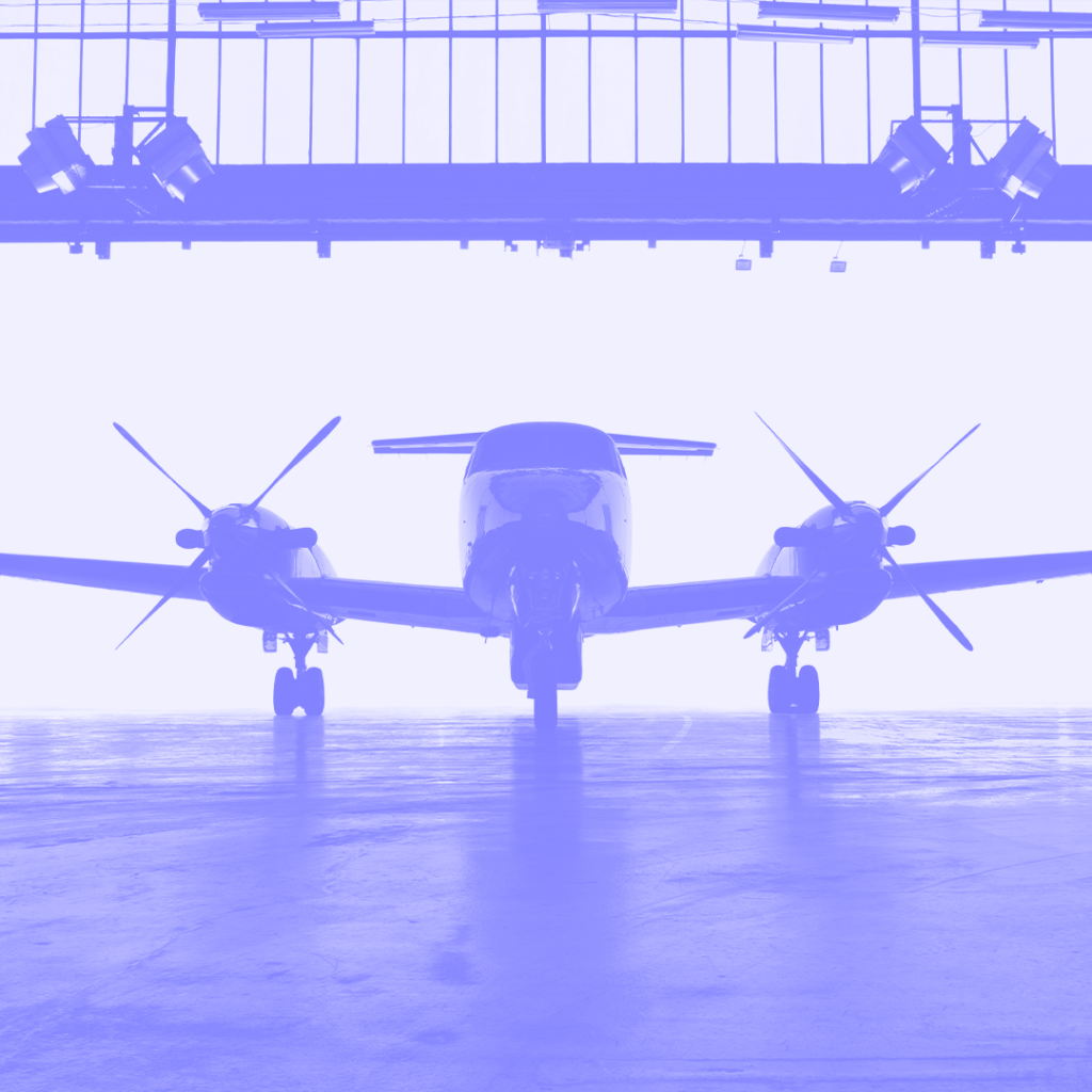 Silhouette of a twin-propeller aircraft inside a hangar, illuminated by soft light from the open doors, emphasizing its readiness for surveillance missions.