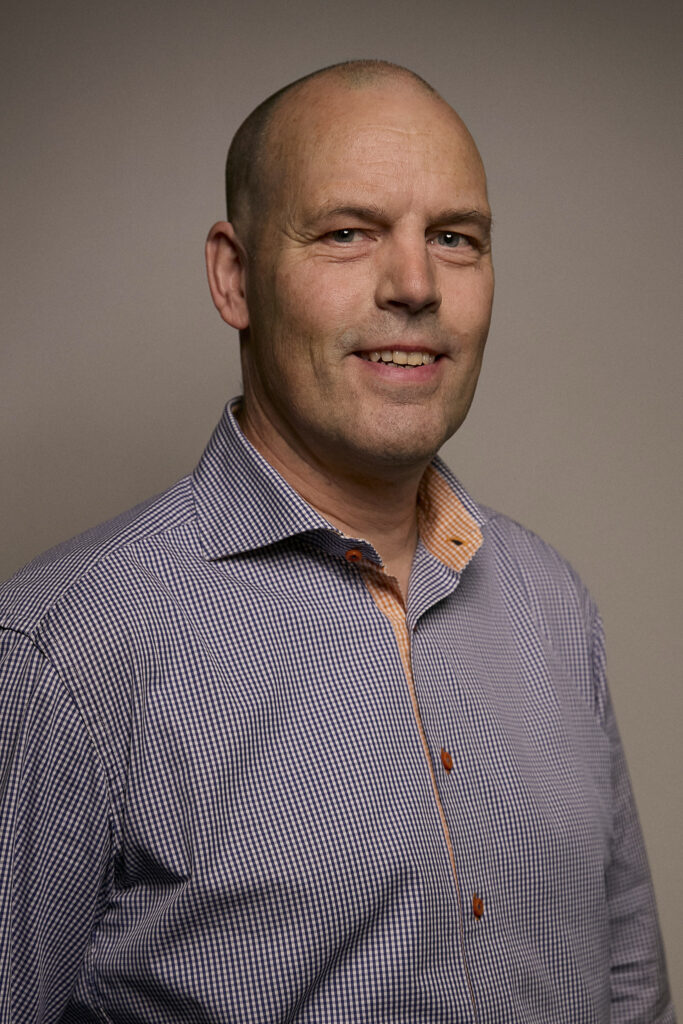 A portrait of a man wearing a checkered shirt, smiling confidently against a neutral background, representing professionalism in airborne surveillance technology.