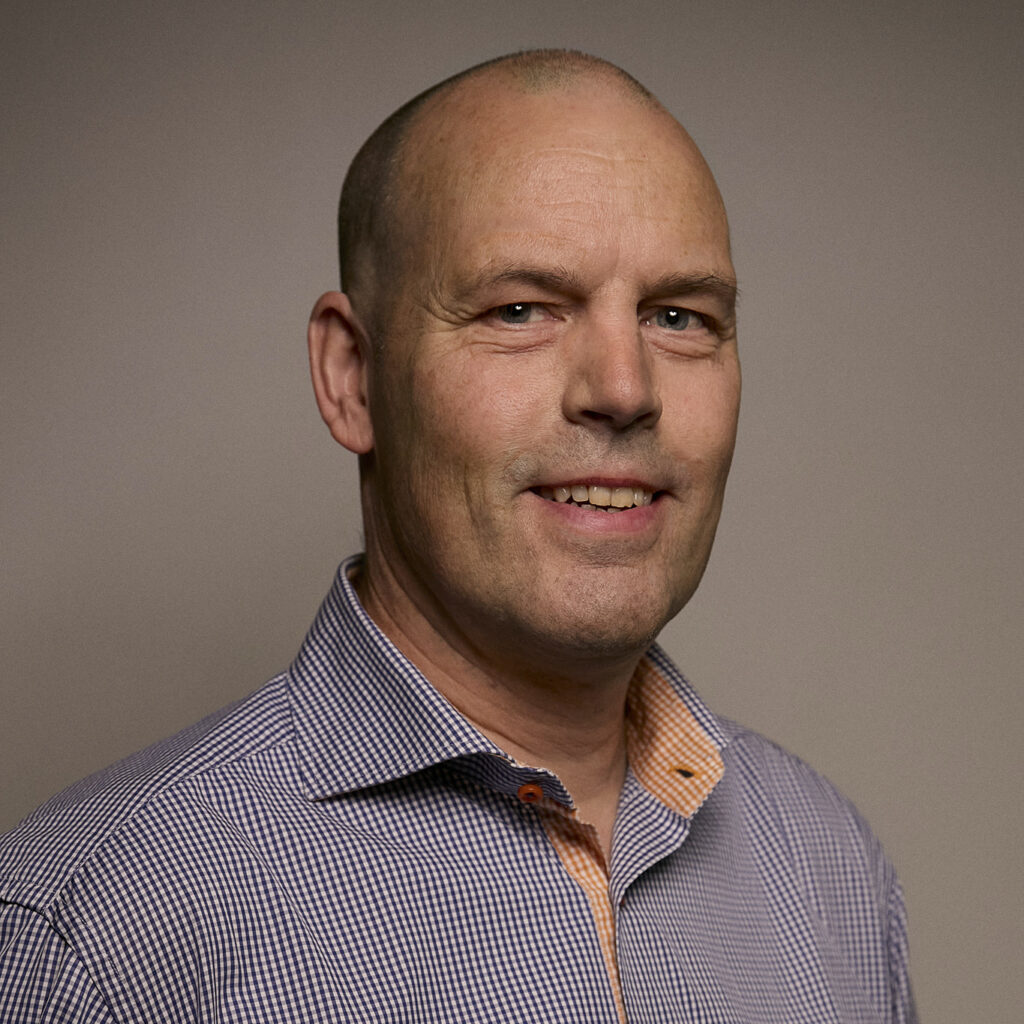 A portrait of a man wearing a checkered shirt, smiling confidently against a neutral background, representing professionalism in airborne surveillance technology.