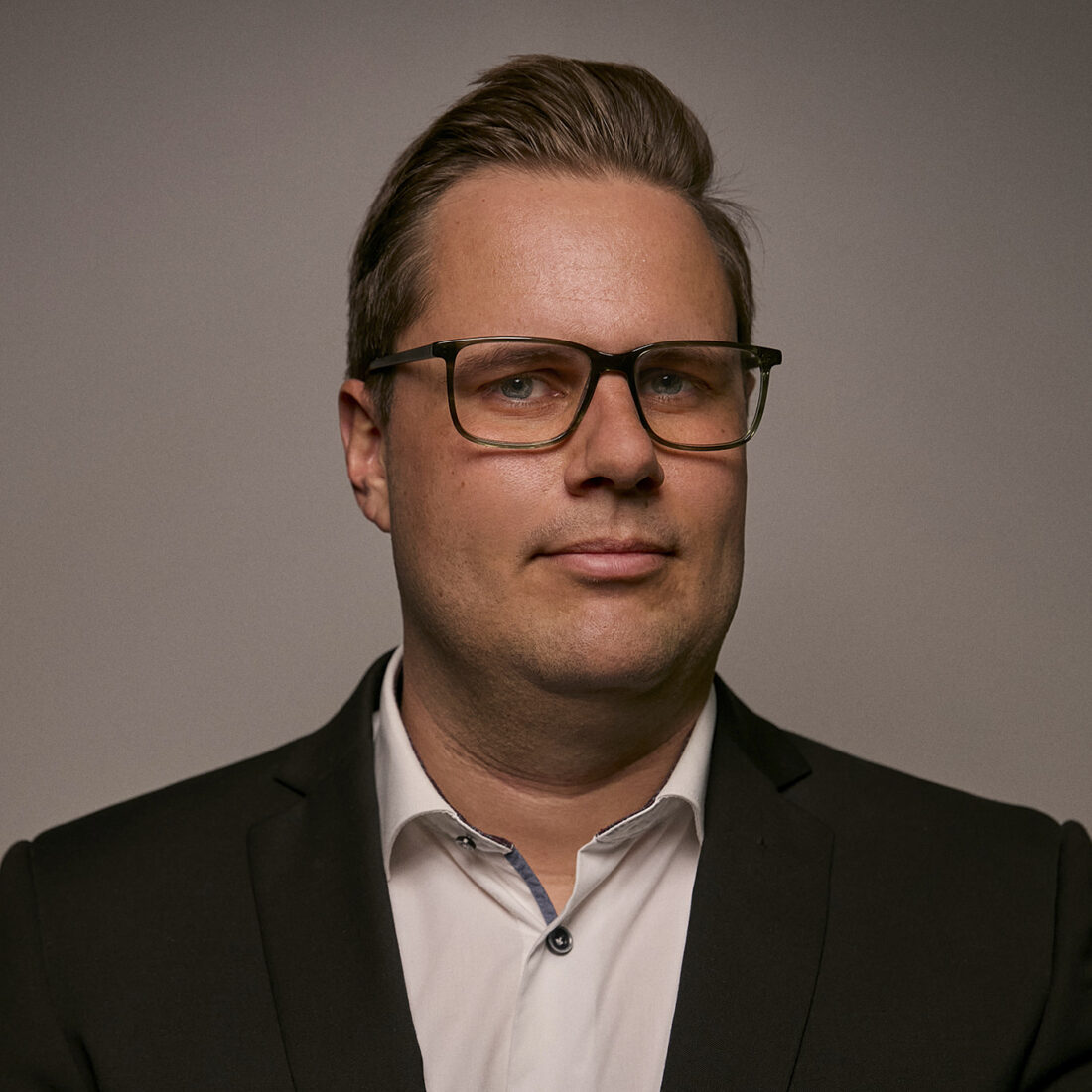 A portrait of a man wearing glasses and a suit, looking confident and professional against a neutral background, representing leadership in airborne surveillance technology.