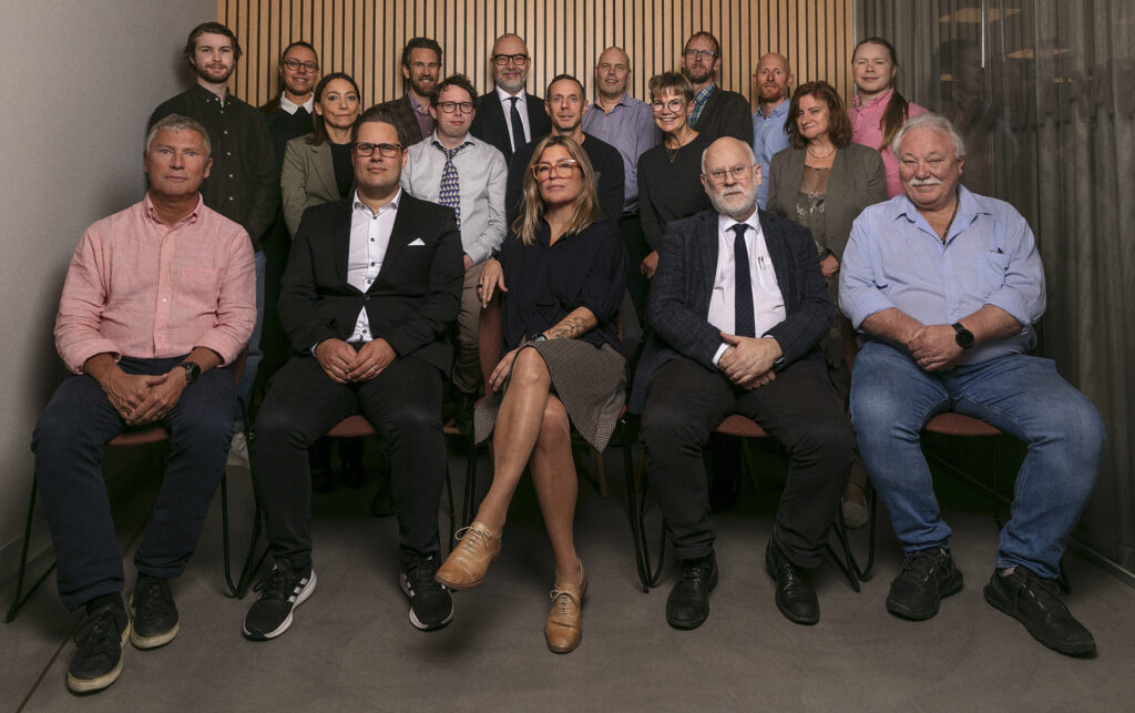 A group photo of a diverse team of professionals seated and standing together in a formal setting, against a wooden panel backdrop, showcasing collaboration and expertise in airborne surveillance technology.